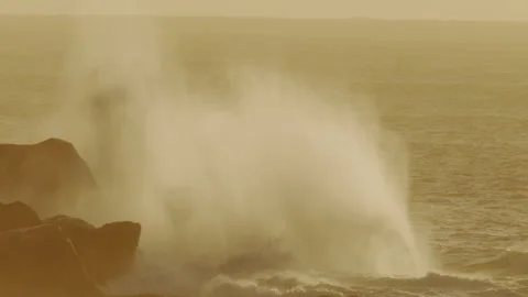 Spray Erupts as Powerful Wave Crashes Into Rocks at Sunset in Amber Light Stock Footage 317879745