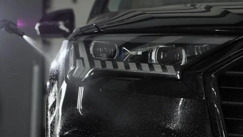 Spraying detergent on the bumper and LED headlight of a modern black car. Video stock 247086740