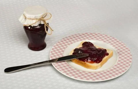 Spread jam on bread Spread jam on bread with knife and jar of jam. Pink ch... Stock Photos