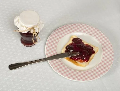 Spread jam on bread Spread jam on bread with knife and jar of jam. Pink ch... Stock Photos