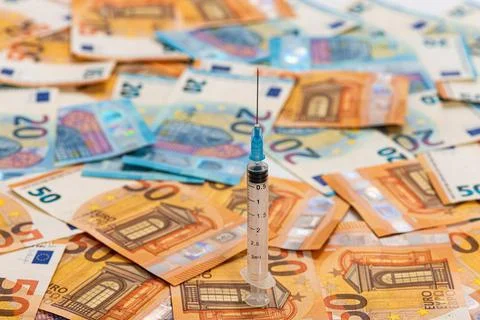 Spread stack of Euro banknotes with syringe on top of them, health costs conc Stock Photos