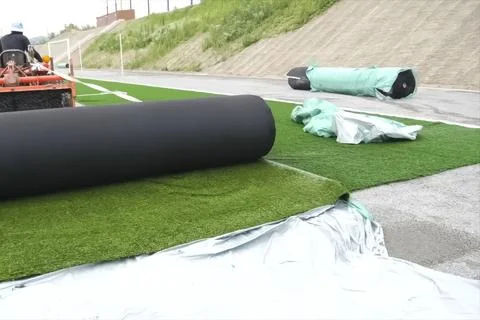 Spreading artificial turf in stadium, rolling out rolls of lawn and leveling. Stock Photos