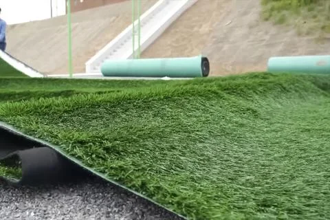 Spreading artificial turf in stadium, rolling out rolls of lawn and leveling. Stock Photos
