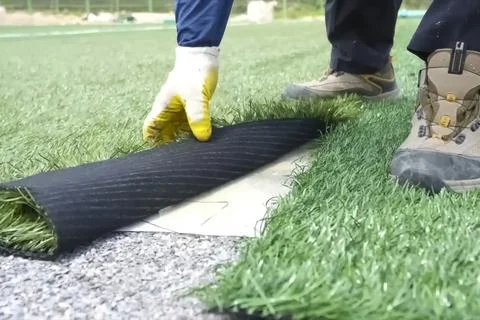 Spreading artificial turf in stadium, rolling out rolls of lawn and leveling. Stock Photos