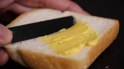 Spreading butter on fresh bread slice with a knife in slow motion on black table Stock Footage 142413839