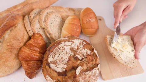 Spreading Butter on Multigrain Bread Slice with Assorted Bakery Items Stock Footage 337533042