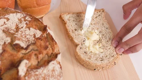 Spreading Butter on Multigrain Bread Slice with Assorted Bakery Items Video stock 337689701