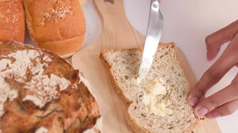 Spreading Butter on Multigrain Bread Slice with Assorted Bakery Loaves Stock Footage 337689729