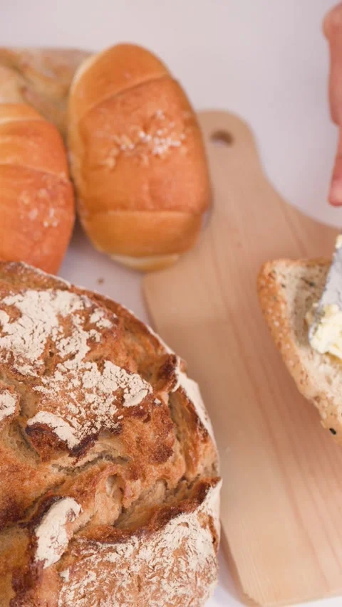 Spreading Butter on Multigrain Bread Slice with Assorted Bakery Loaves Stock Footage 337689832