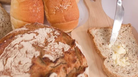 Spreading Butter on Multigrain Bread Slice with Assorted Bakery Items Video stock 337770698