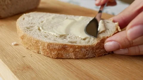 Spreading cheese with knife. Breakfast prep. Rustic style. Stock Footage 308397338