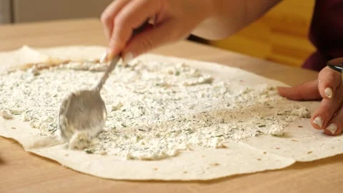 Spreading cheese mixture on rolled pita bread. Preparing a pita dish. Stock Footage 316036434