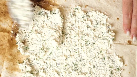 Spreading cheese mixture on rolled pita bread. Preparing a pita dish. Stock Footage 316037129