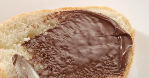 Spreading chocolate hazelnut spread on bread by knife. Angle view. Stock Footage 243773786