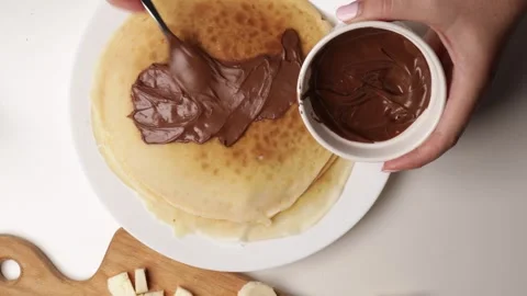 Spreading chocolate paste on stack of pancakes using spoon. overhead close-up of Stock Footage 316472613
