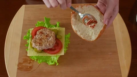 Spreading condiment on bread slice during burger assembly, wooden counter Stock Footage 345060469