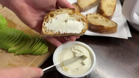 Spreading cream cheese on crispy bread with avocado nearby Stock-Footage 310502101