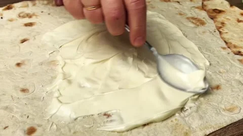 Spreading creamy mayonnaise on fresh flatbread with a spoon for delicious snack Stock Footage 325032454