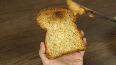 Spreading creamy organci peanut butter on whole wheat bread Stock Footage