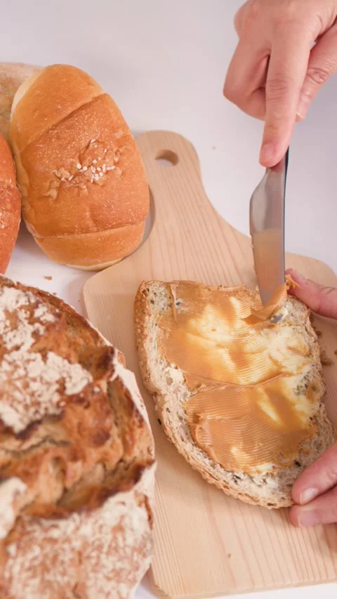 Spreading Creamy Peanut Butter on Multigrain Bread Slice with Knife Stock Footage 337533101