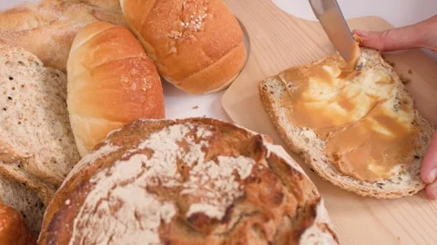 Spreading Creamy Peanut Butter on Multigrain Bread with Assorted Loaves Video stock 337689636