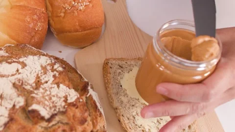 Spreading Creamy Peanut Butter on Multigrain Bread with Assorted Loaves Video stock 337768642