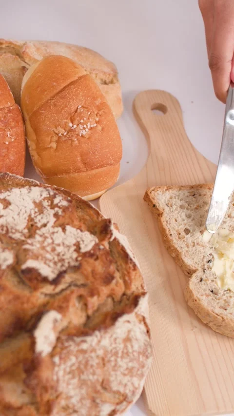 Spreading Creamy Peanut Butter on Multigrain Bread with Assorted Loaves Video stock 337860320