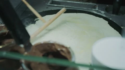 Spreading crepe batter on a hot griddle with a wooden tool in a kitchen setting. Stock Footage 314084650