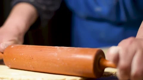 Spreading flour on a rolling pin surface with a hand above raw dough in round Stock Footage 130525463