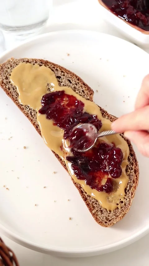 Spreading fruit jam on top bread slice with peanut butter 스톡 동영상 310803101