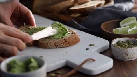Spreading guacamole on a rye bread toast. Healthy eating concept. Stock Footage 124329074