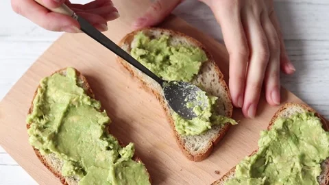 Spreading guacamole on whole grain bread, making a vegan healthy breakfast Stock Footage 151748076