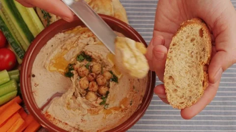 Spreading hummus on bread top view. Hummus garnished with chickpeas, olive oil Stock Footage 262578403