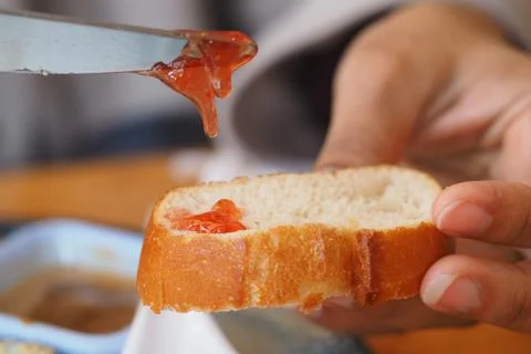 Spreading jam on a slice of bread in the kitchen Stock Photos