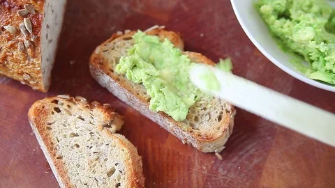 Spreading mashed avocado on artisan bread 스톡 동영상 77811305