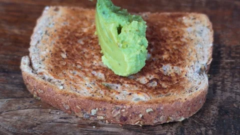 Spreading mashed avocado on whole grain toast for healthy breakfast Stock Footage 348488613