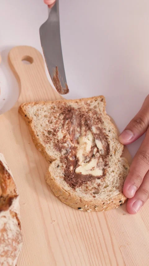 Spreading Nut Butter on Multigrain Bread Slice on Wooden Board Video stock 337770985