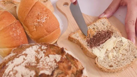 Spreading Peanut Butter on Multigrain Bread with Assorted Bakery Loaves Video stock 337533092