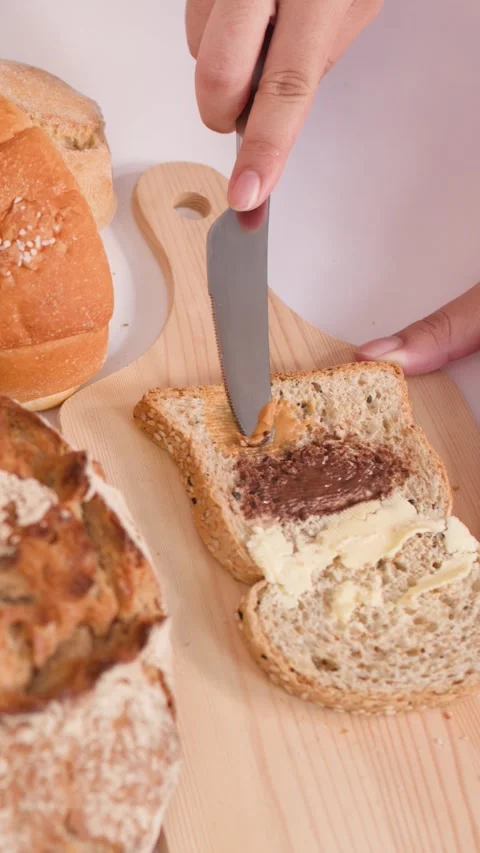 Spreading Peanut Butter on Multigrain Bread with Assorted Bakery Loaves Video stock 337768011