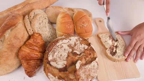 Spreading Peanut Butter on Multigrain Bread with Assorted Bakery Items Stock Footage 337769008