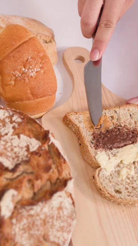 Spreading Peanut Butter on Sliced Bread with Assorted Bakery Loaves Video stock 337748623