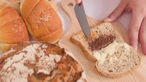 Spreading Peanut Butter on Sourdough Bread with Assorted Bakery Items Video stock 337746856