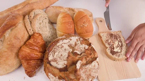 Spreading Peanut Butter on Sourdough Slice with Assorted Bakery Breads Stock Footage 337691037