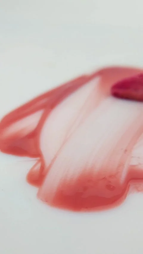 Spreading red or pink lip tint evenly on a white background using a brush. .. Stock Footage 332227174