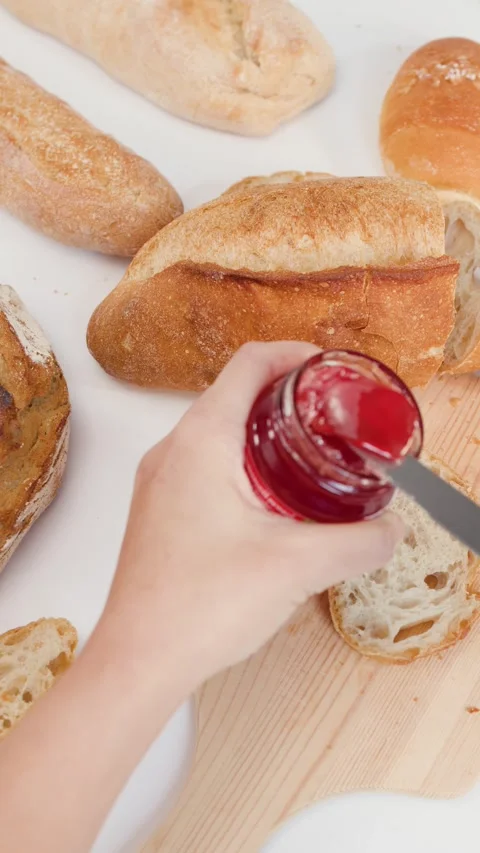 Spreading Red Strawberry Jam on Sliced Sourdough Bread for Breakfast Stock Footage 337532967