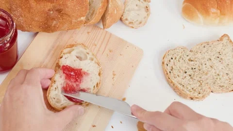 Spreading Red Strawberry Jam on Sliced Sourdough Bread for Breakfast Stock Footage 337535571