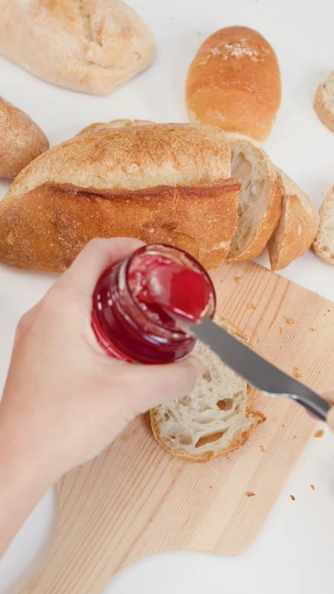Spreading Red Strawberry Jam on Sliced Sourdough Bread for Breakfast Stock Footage 337767970