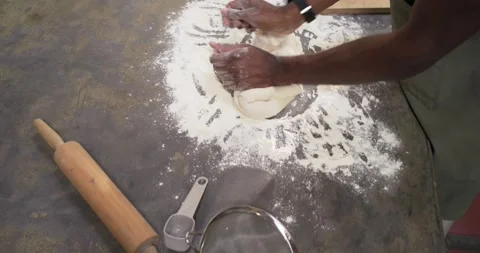 Spreading ring of flour, African man in green apron kneading dough for baking at Video stock 345072470