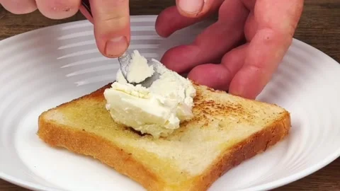 Spreading soft cream cheese on toasted bread slice with a spoon for breakfast Stock Footage 324943449
