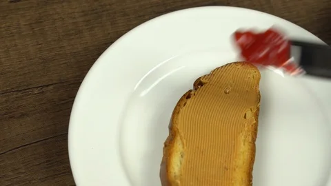 Spreading strawberry jam on top of peanut butter bread Stock Footage 113074898
